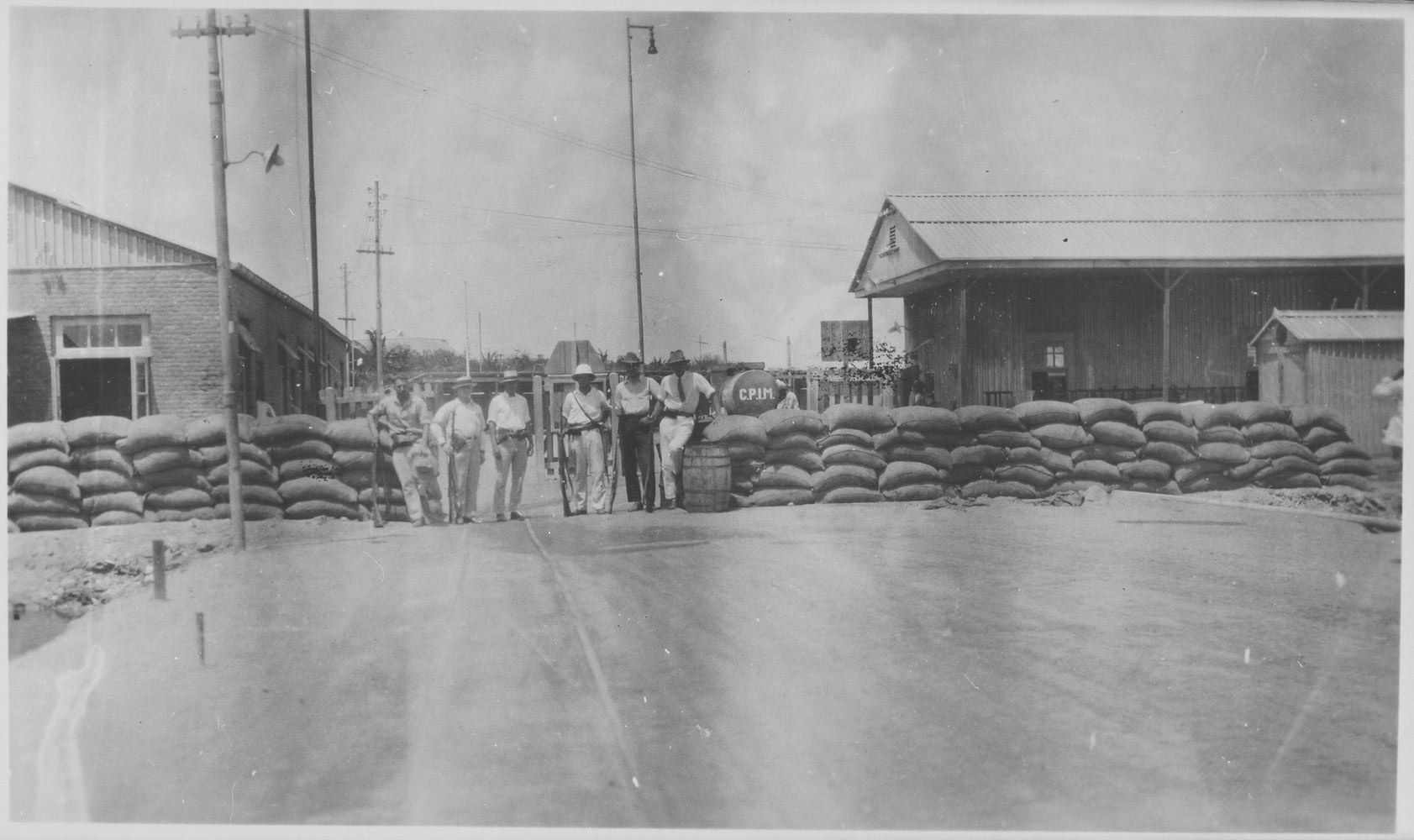 Armed CPIM employees and police officers guard the gates of labor housing camps around the Isla Refinery after an uprising in 1929. The images illustrate how camp architecture benefits surveillance. 