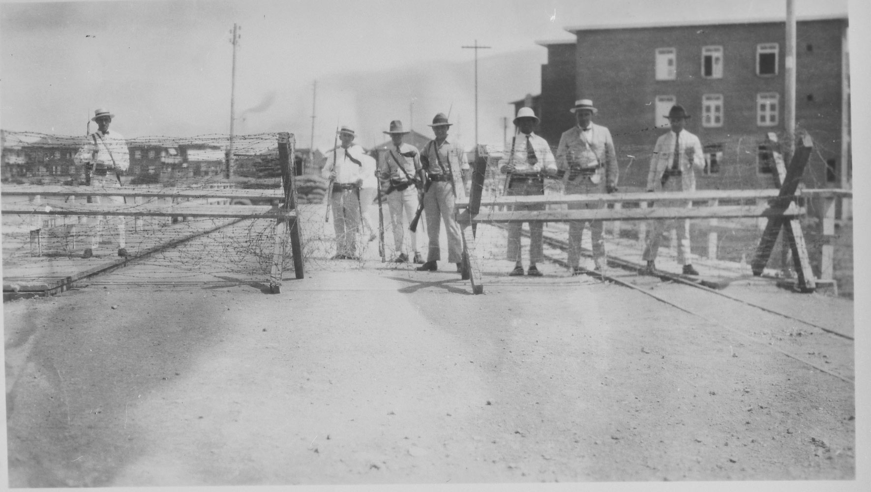 Armed CPIM employees and police officers guard the gates of labor housing camps around the Isla Refinery after an uprising in 1929. The images illustrate how camp architecture benefits surveillance. 
